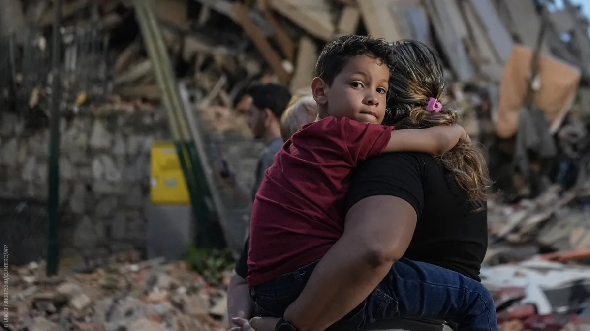 criança no colo na frente de escombros pós terremoto