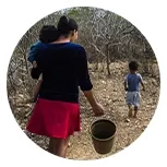 mulher com criança no colo com balde na mão no caminho para buscar agua