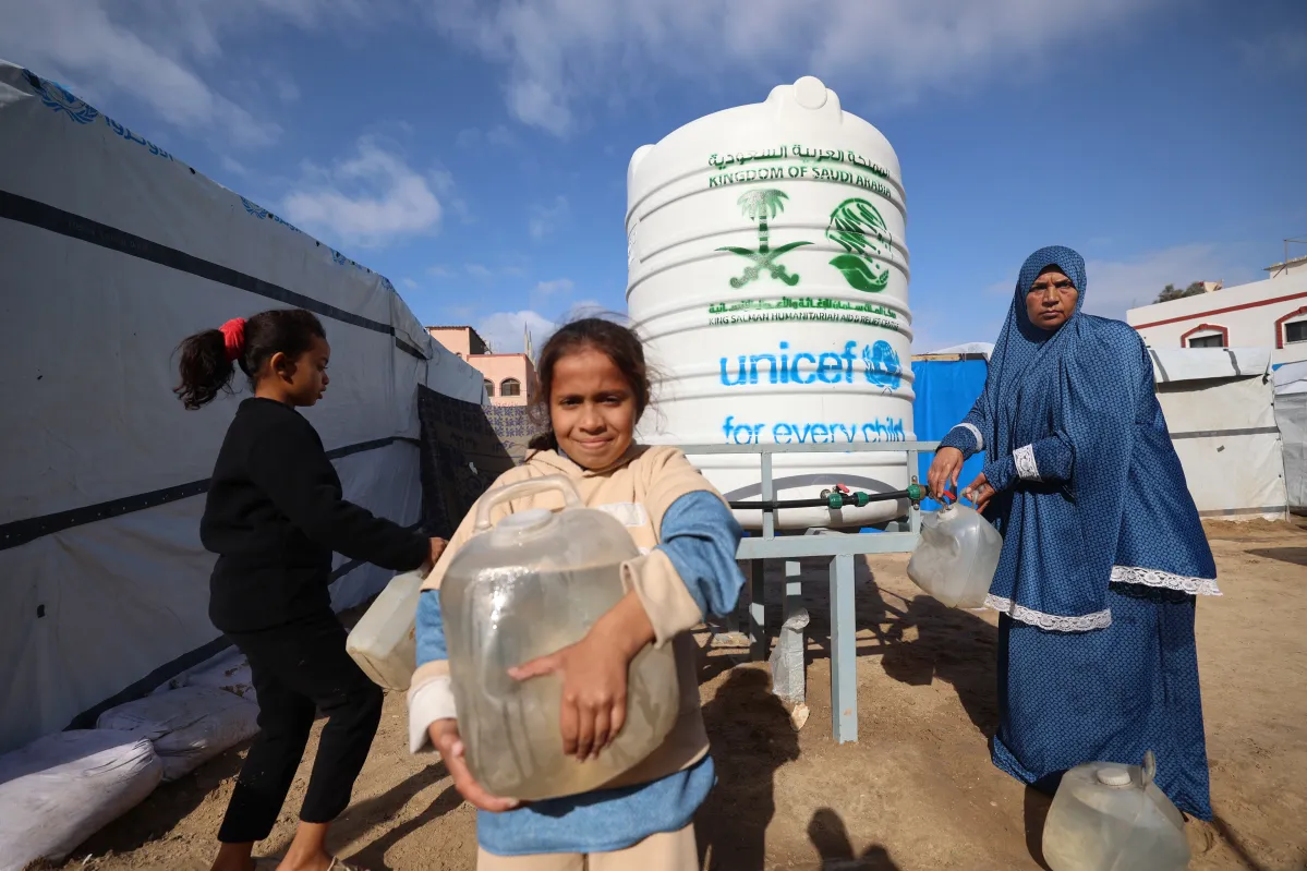 Niña carga un bidón de agua frente a un tanque de UNICEF, parte de respuesta humanitaria en Gaza. 