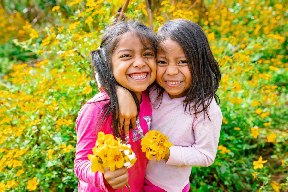 Niñas sonríe a la cámara con flores en la mano. Programas UNCIEF.