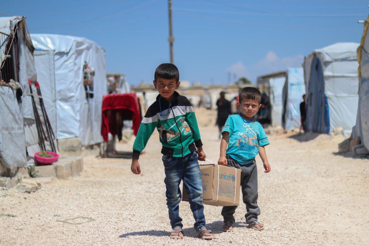 On 29 April 2020 in the Syrian Arab Republic, brothers Ahmad (left), 7, and Saad, 5, help their mother carry their newly received family hygiene kit back to their tent in Fafin camp, northern rural Aleppo.