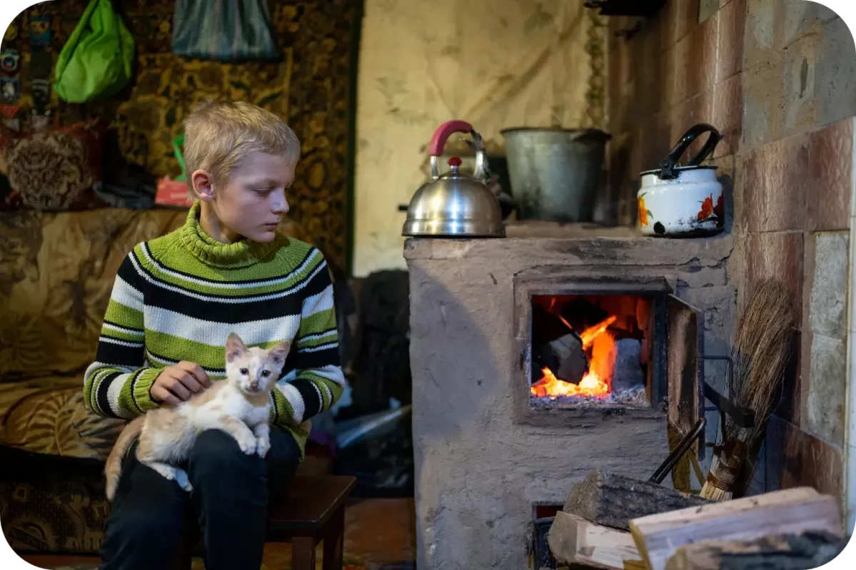 Ten-year-old Bohdan with a cat, near the oven in his broken brick house, where he lives with his grandmother and two sisters.