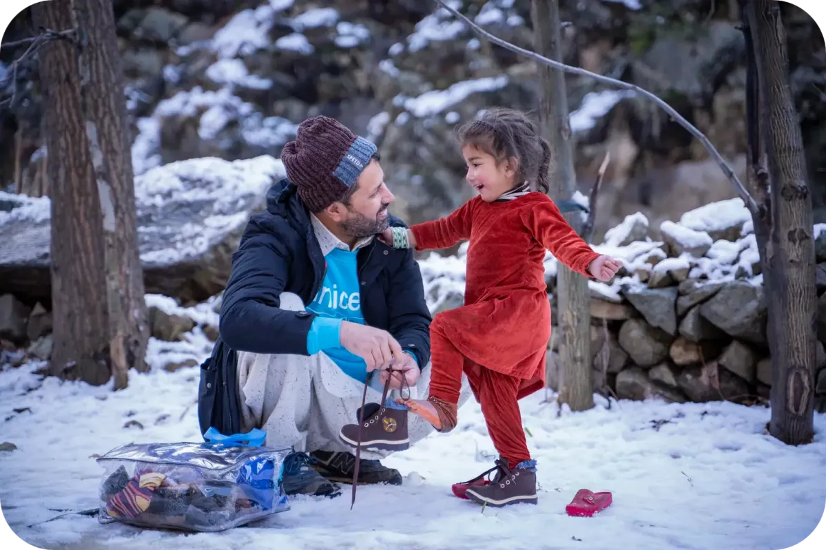 UNICEF Planning, Monitoring and Evaluation Officer - Zaheer Ahmad helps 3-year-old Muskan wear shoes which were part of the winter kit provided to her by UNICEF in Sulool Daramdala village, Upper Dir District, Khyber Pakhtunkhwa. 