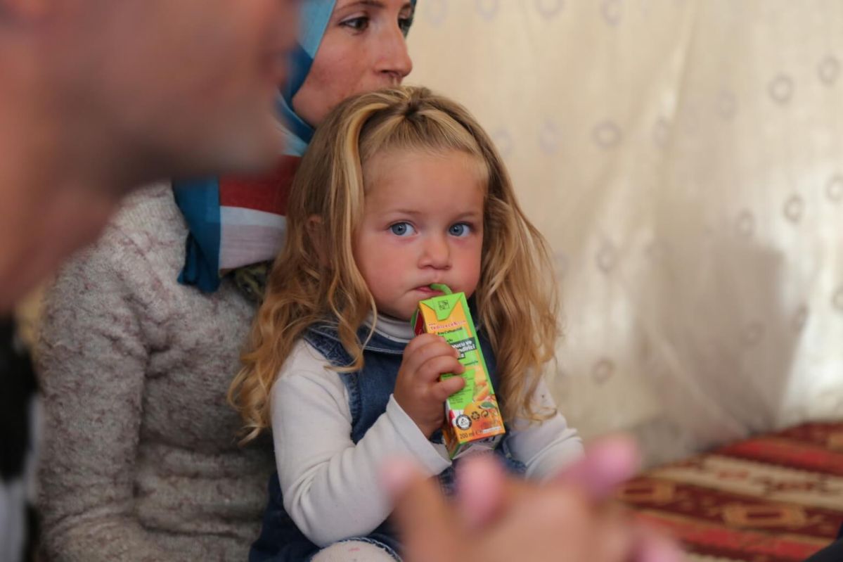 A Syrian girl looks while sitting in her mother's lap in her family's tent in Suruc Camp