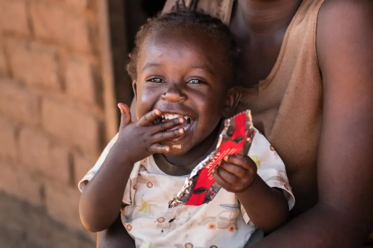 20-year-old Edna Maunde smiles as her daughter, 2 year 4 months old Christina Cosmas eats RUTF at their home in Mavila Village, Zomba, southern Malawi on Thursday, 8 June 2023. 