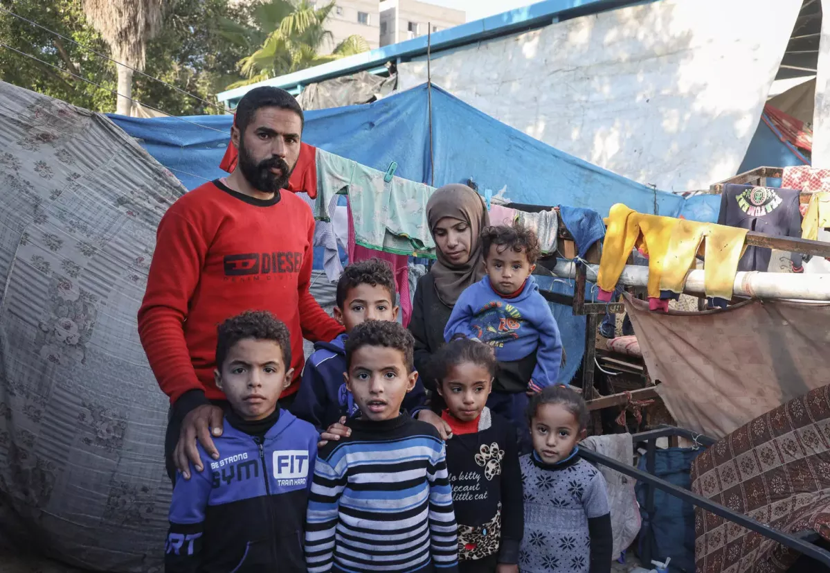 On 19 December 2023, in a shelter for internally displaced persons in Rafah, southern Gaza Strip, Mahmoud and his wife Eman pose for a photograph with their children.