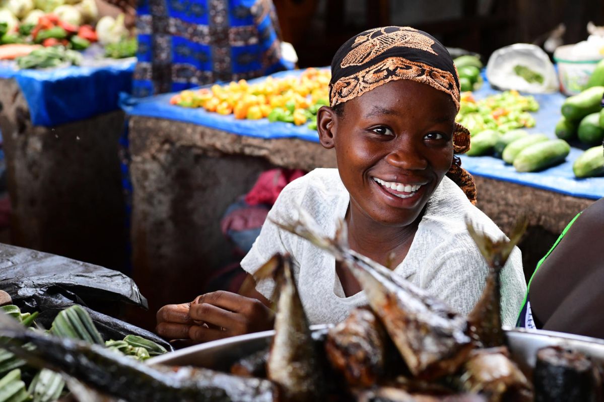 A woman smiling as she sells fish and vegetables in the market