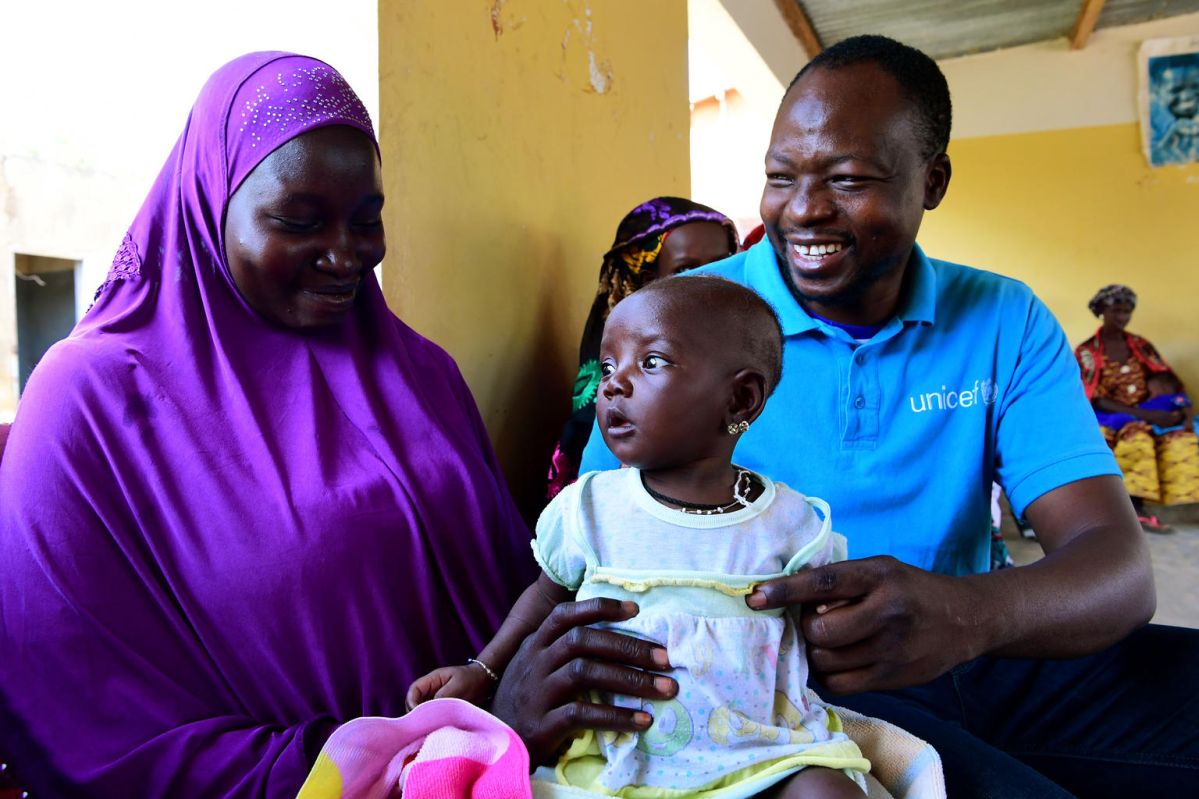 A UNICEF staff with a mother and her child, all smiling