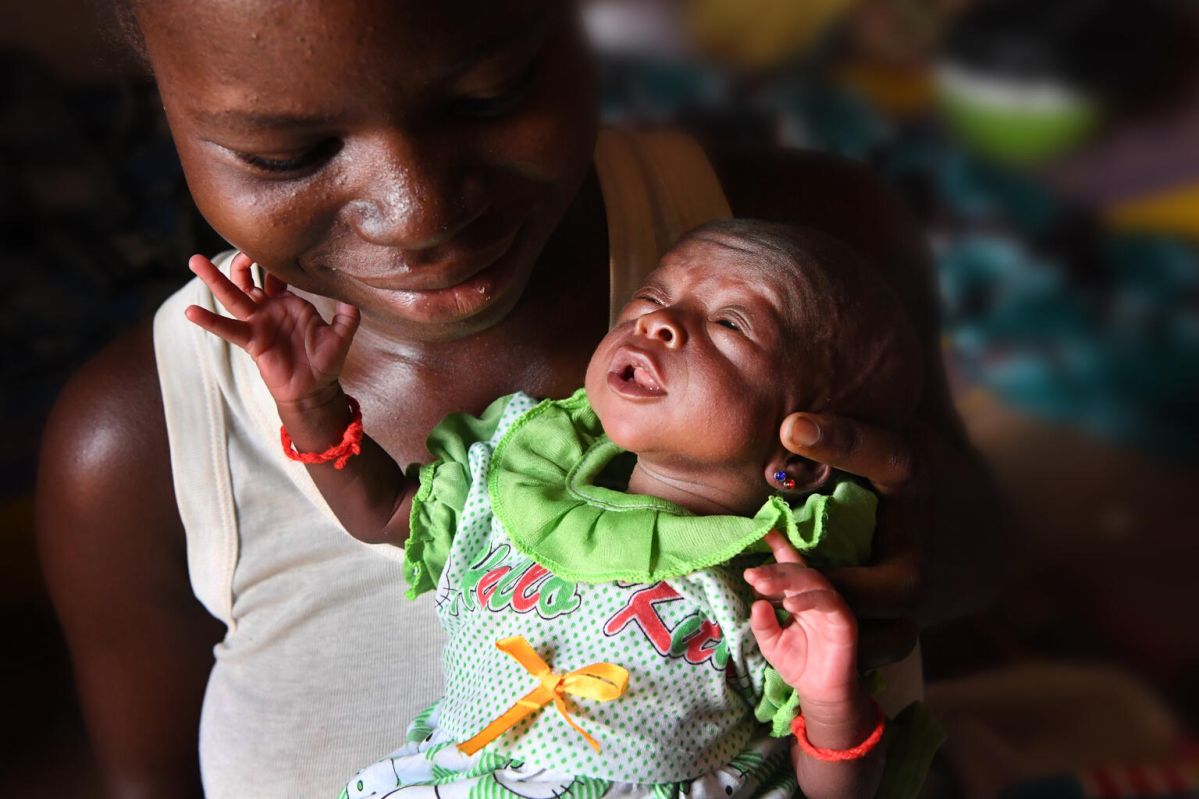 A mother smiling while carrying her newborn baby