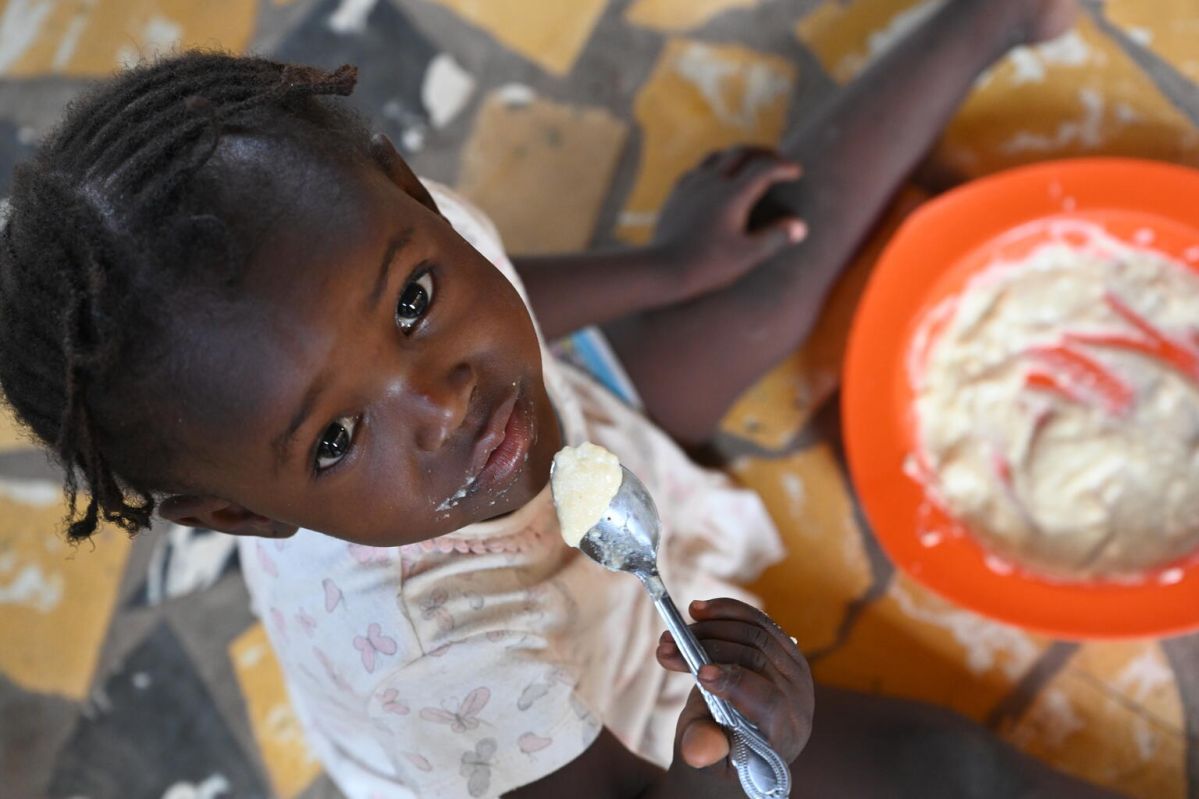 A little girl sitting on the floor and eating from a place